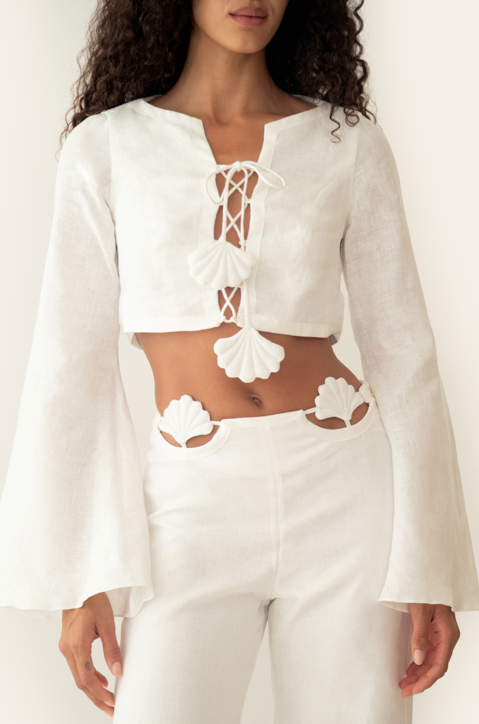 Azulu Amelia Top front detail, lace-up flower fastenings and shell appliques on the cropped white linen shirt worn with matching trousers