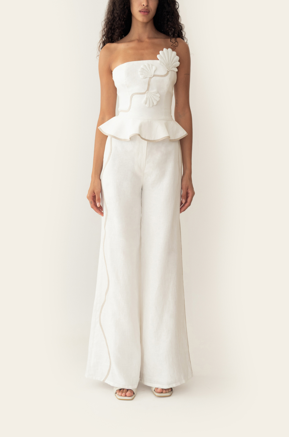 Azulu Vaiana Pants and Vaiana Top in white linen, front view of the strapless peplum top with floral applique above high-waisted wide-leg trousers