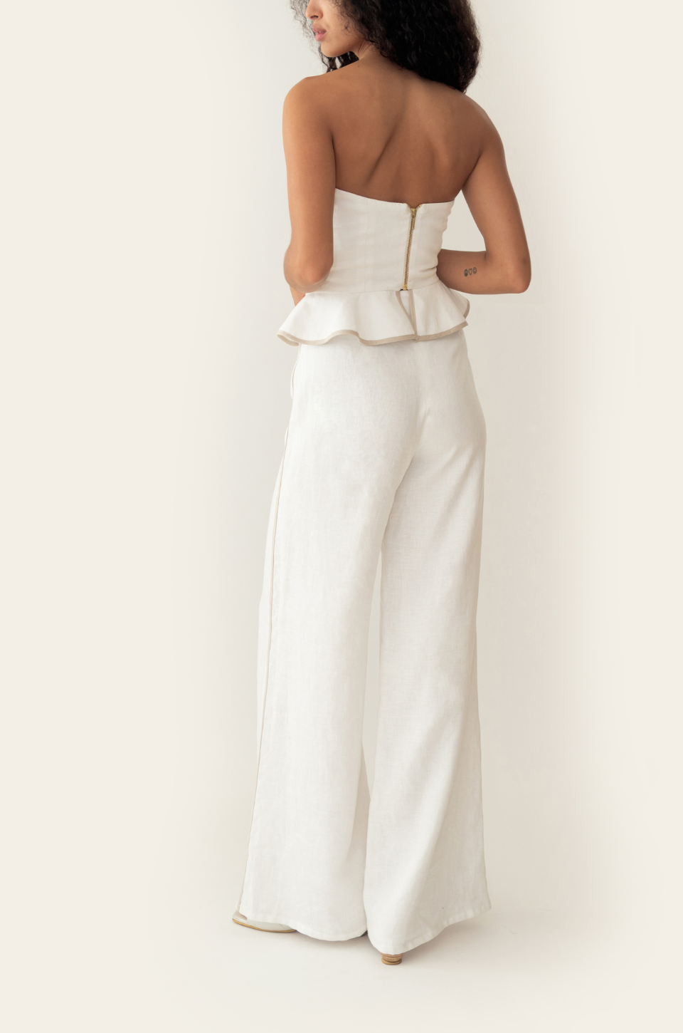 Azulu Vaiana Pants back view, white linen wide-leg trousers falling straight to the floor beneath the ruffled peplum top