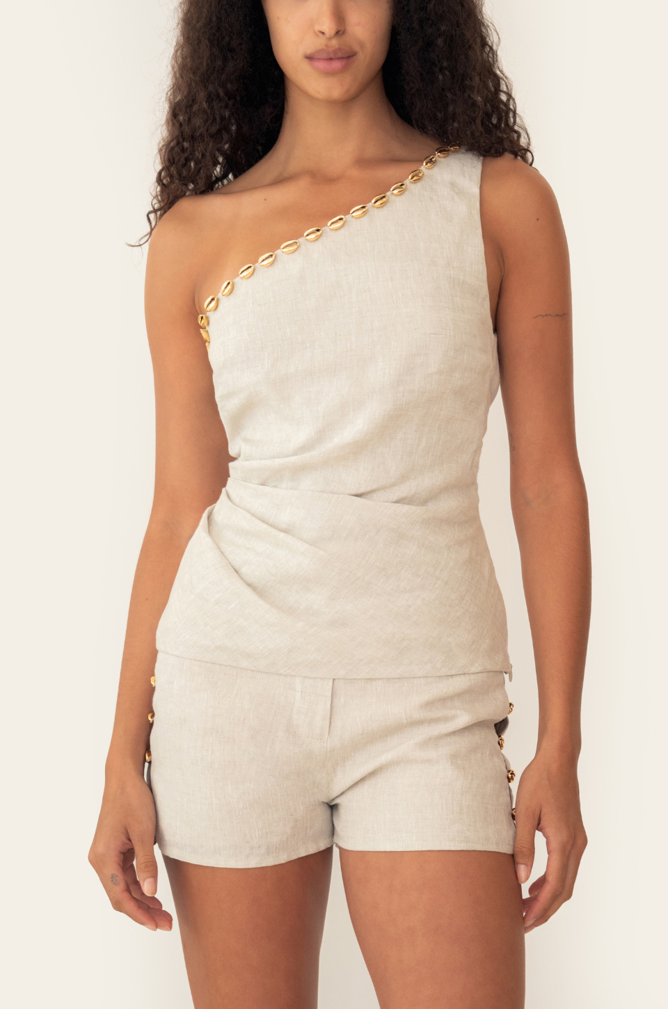 Azulu Eda Top and Eda Short in sand linen, front view of the one-shoulder top with gold beaded chain neckline over the matching tailored short